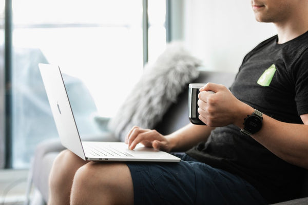 Man sitting on couch using laptop computer and holding coffee